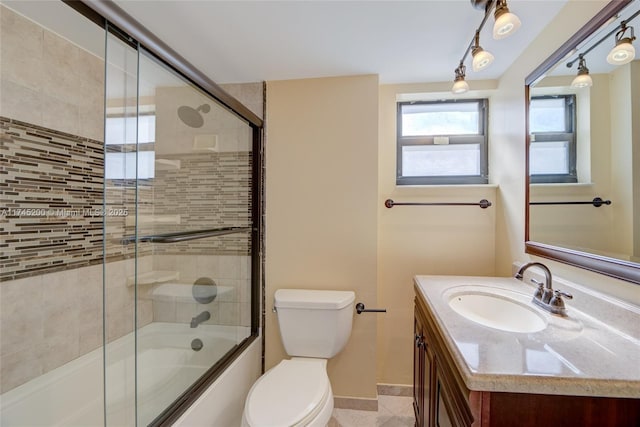 full bath featuring baseboards, vanity, toilet, and bath / shower combo with glass door