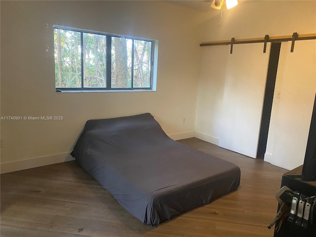 bedroom featuring a barn door, baseboards, and dark wood-style flooring