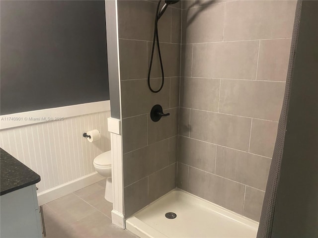 full bath with a stall shower, toilet, a wainscoted wall, tile patterned floors, and vanity