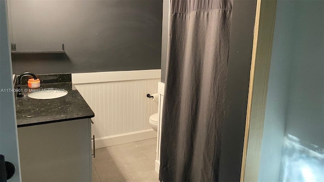 full bathroom with a wainscoted wall, vanity, toilet, and tile patterned floors