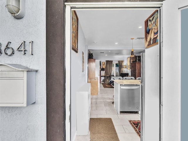 kitchen featuring pendant lighting, light tile patterned floors, stainless steel dishwasher, and white cabinets