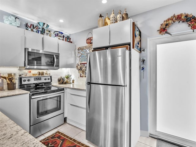 kitchen with appliances with stainless steel finishes, white cabinetry, backsplash, light tile patterned floors, and light stone counters