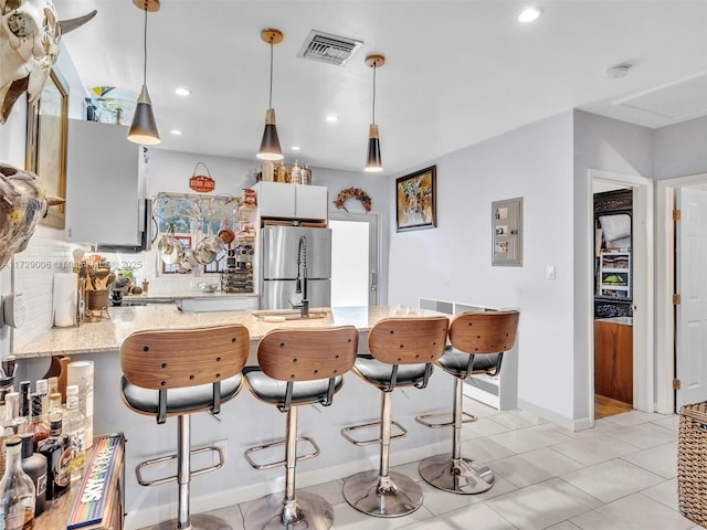 kitchen with electric panel, light stone countertops, stainless steel fridge, and decorative light fixtures