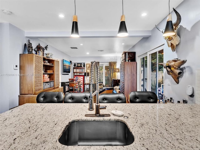 interior space with light stone counters, hanging light fixtures, beam ceiling, and sink