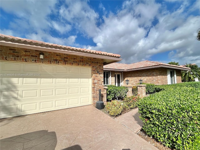 view of front of property with driveway, brick siding, an attached garage, and a tile roof