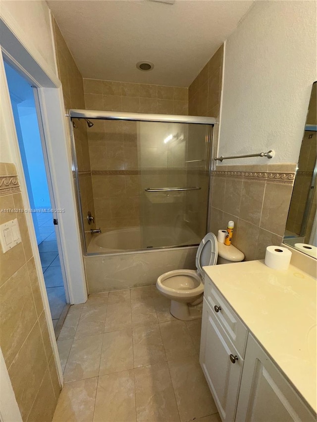 full bathroom with tile walls, shower / bath combination with glass door, tile patterned flooring, vanity, and toilet