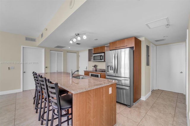 kitchen with a kitchen island with sink, stainless steel appliances, a breakfast bar, sink, and light stone counters