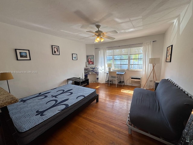 bedroom featuring hardwood / wood-style floors, a wall unit AC, and ceiling fan