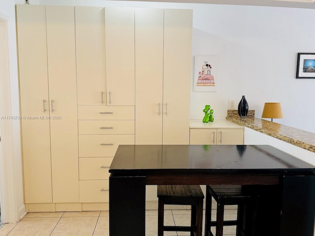 kitchen featuring white cabinetry, light stone countertops, kitchen peninsula, and light tile patterned flooring