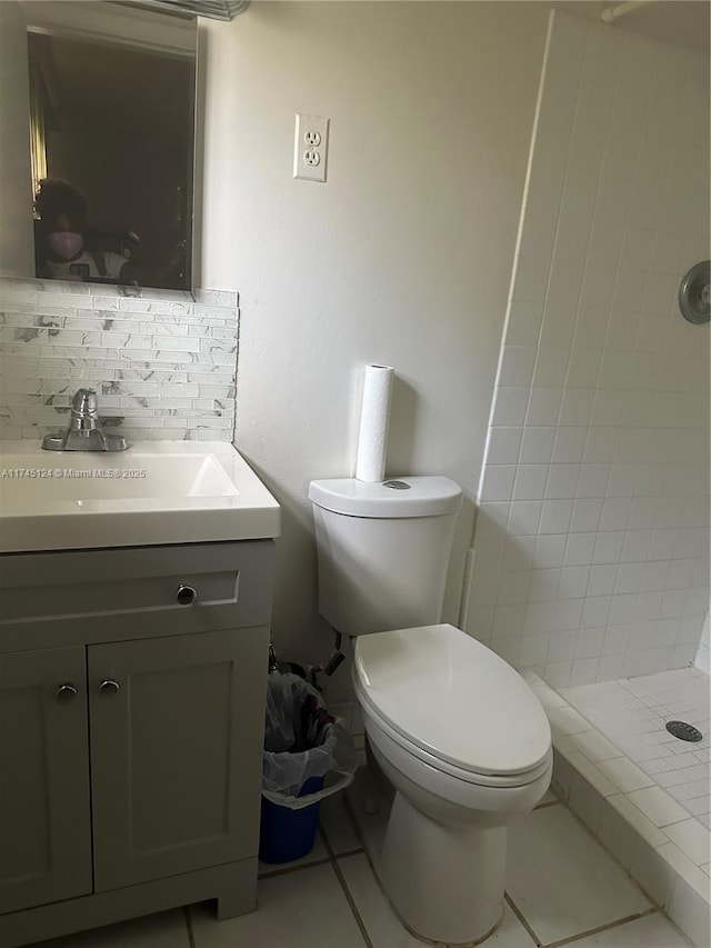 bathroom with toilet, a tile shower, vanity, tile patterned flooring, and decorative backsplash