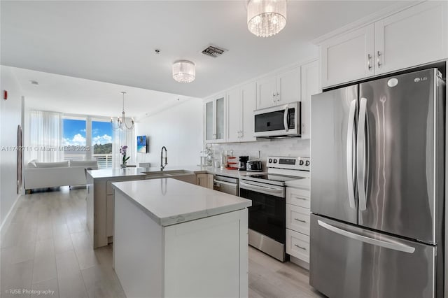 kitchen with pendant lighting, sink, stainless steel appliances, white cabinets, and kitchen peninsula