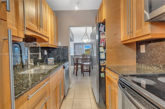 kitchen with sink, light tile patterned floors, appliances with stainless steel finishes, dark stone countertops, and decorative backsplash