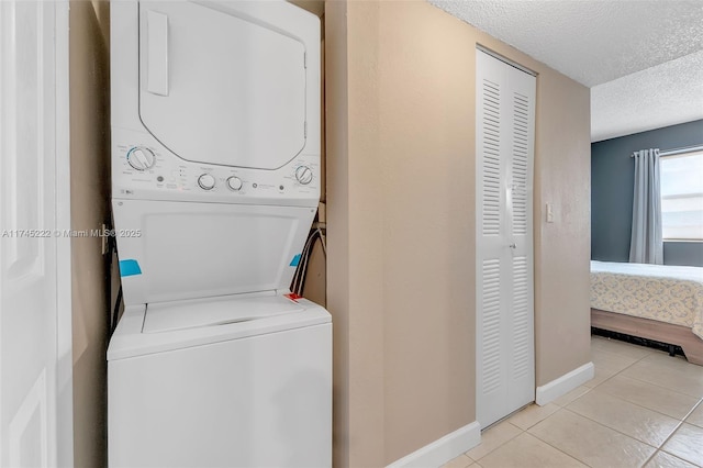 laundry room featuring stacked washer / drying machine, a textured ceiling, and light tile patterned floors