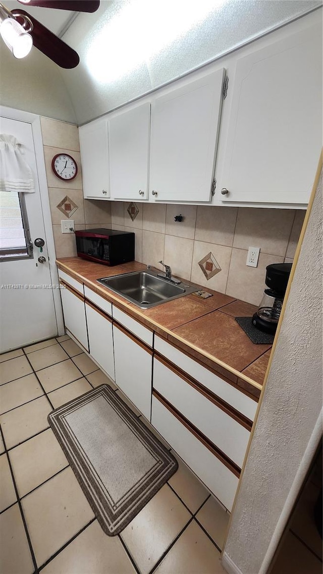 kitchen featuring black microwave, white cabinetry, a sink, and backsplash