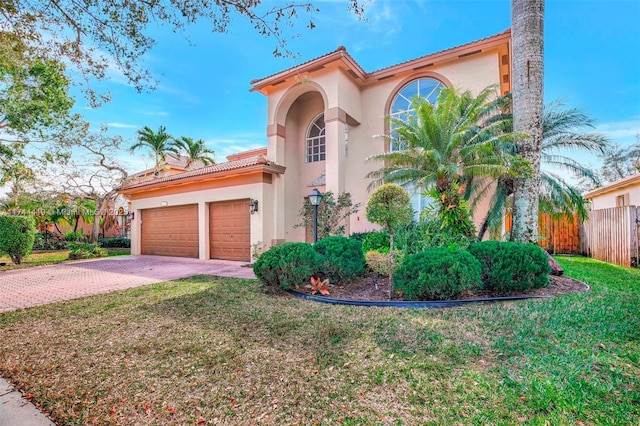 mediterranean / spanish-style house with decorative driveway, stucco siding, fence, a garage, and a front lawn