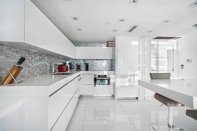 kitchen with sink, white cabinetry, stainless steel oven, light tile patterned floors, and backsplash