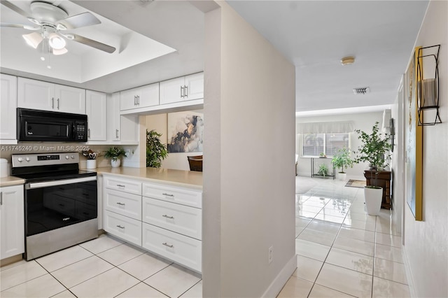 kitchen with stainless steel electric range oven, white cabinets, light tile patterned floors, ceiling fan, and a tray ceiling