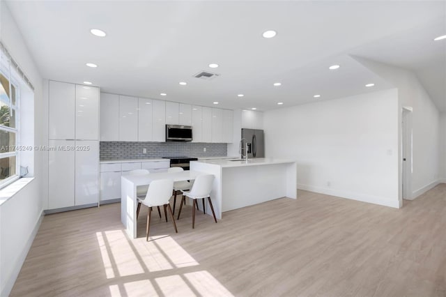 kitchen with a kitchen bar, a center island with sink, stainless steel appliances, decorative backsplash, and white cabinets