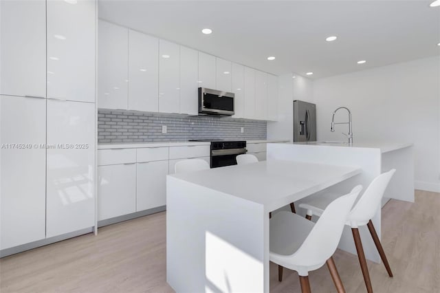 kitchen with sink, light hardwood / wood-style flooring, white cabinetry, stainless steel appliances, and a kitchen bar