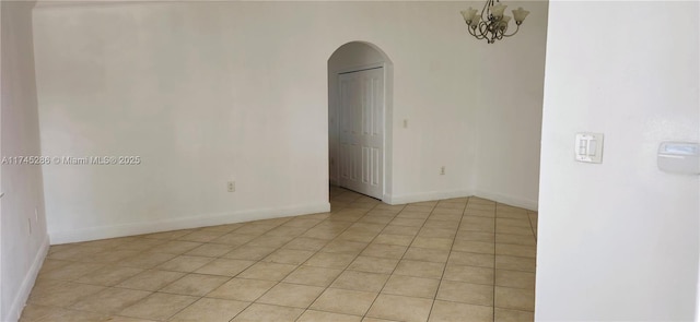 tiled spare room with a notable chandelier