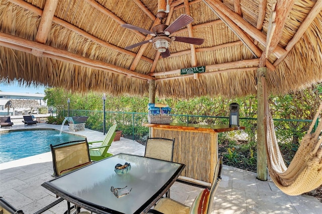 view of patio / terrace featuring a fenced in pool, ceiling fan, a gazebo, a bar, and pool water feature