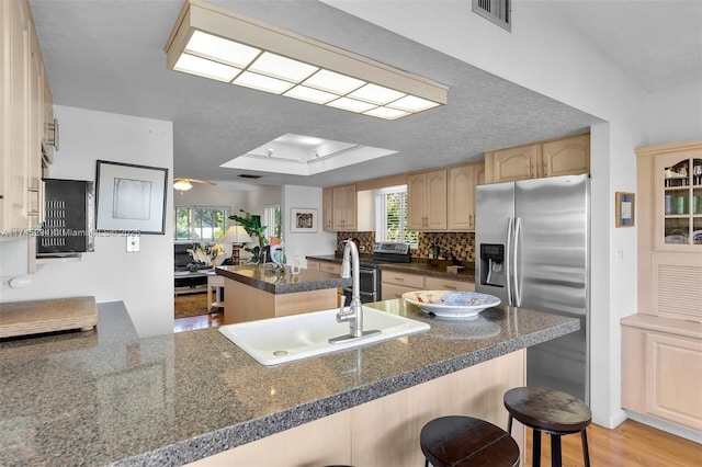 kitchen with sink, a breakfast bar area, appliances with stainless steel finishes, a raised ceiling, and kitchen peninsula