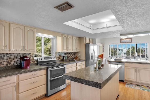 kitchen with sink, stainless steel appliances, light hardwood / wood-style floors, a kitchen island, and a raised ceiling