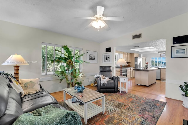 living room with ceiling fan, a textured ceiling, and light hardwood / wood-style flooring