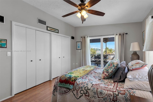 bedroom with a textured ceiling, light hardwood / wood-style flooring, two closets, ceiling fan, and access to exterior