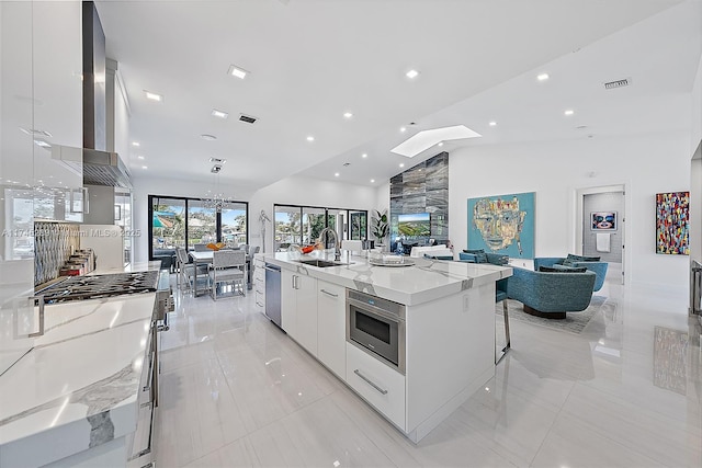 kitchen with dishwasher, white cabinetry, sink, a large island, and light stone countertops