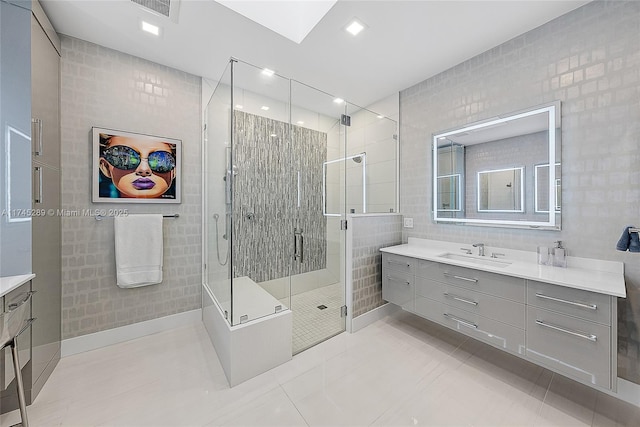 bathroom featuring a skylight, vanity, tile walls, and a shower with shower door