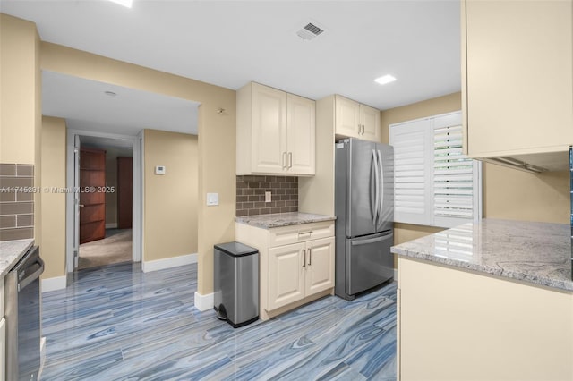 kitchen with dishwashing machine, decorative backsplash, light stone countertops, and stainless steel refrigerator