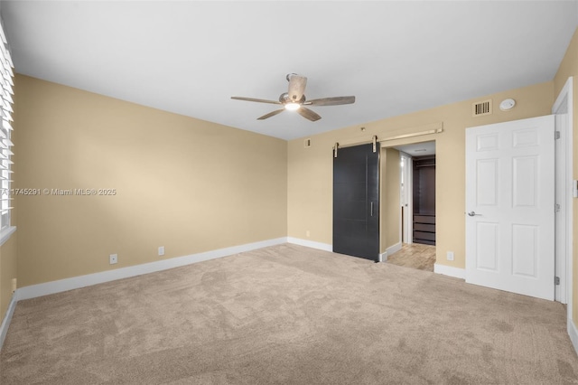 unfurnished bedroom featuring light colored carpet, a barn door, and ceiling fan