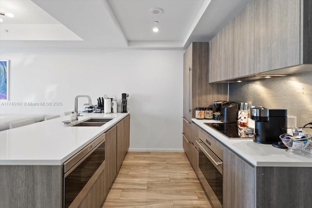 kitchen with sink, black electric stovetop, a tray ceiling, decorative backsplash, and stainless steel oven