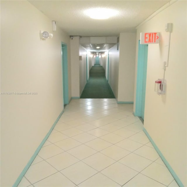 corridor featuring a textured ceiling, light tile patterned flooring, and baseboards