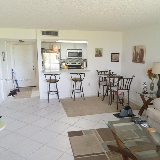 kitchen featuring visible vents, decorative backsplash, a breakfast bar, a peninsula, and stainless steel appliances