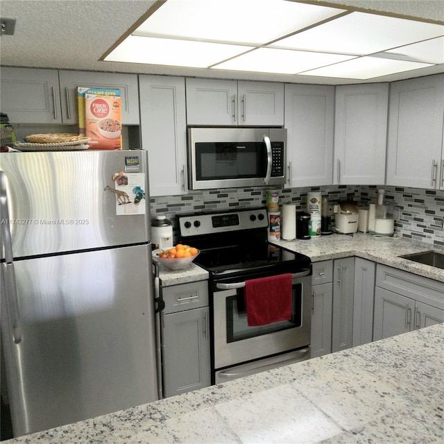 kitchen featuring stainless steel appliances, gray cabinets, light stone countertops, and decorative backsplash