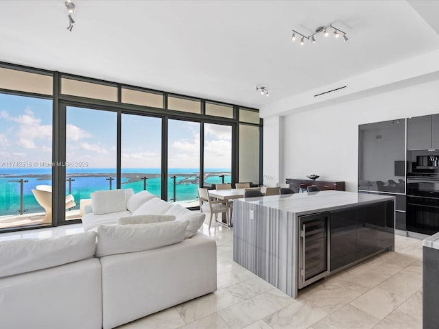 living room featuring track lighting, beverage cooler, expansive windows, and a water view