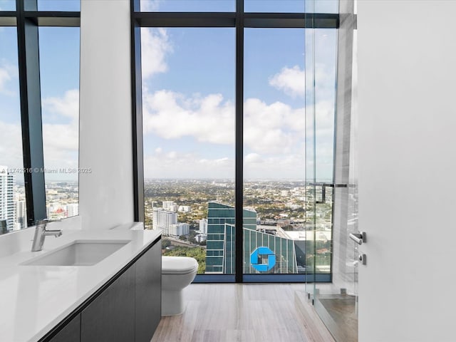 bathroom featuring expansive windows, vanity, hardwood / wood-style flooring, and toilet