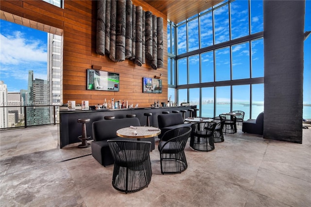 bar featuring floor to ceiling windows, a towering ceiling, wood ceiling, and wooden walls