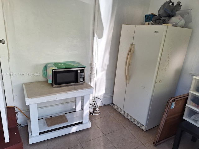 kitchen featuring tile patterned flooring, stainless steel microwave, light countertops, and freestanding refrigerator