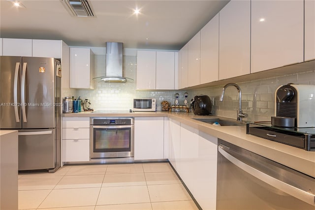 kitchen with wall chimney exhaust hood, sink, light tile patterned floors, stainless steel appliances, and white cabinets