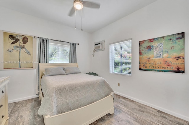 bedroom with hardwood / wood-style flooring, an AC wall unit, and ceiling fan