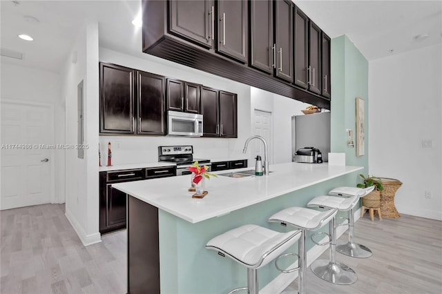 kitchen with sink, light hardwood / wood-style flooring, a breakfast bar, stainless steel appliances, and dark brown cabinetry