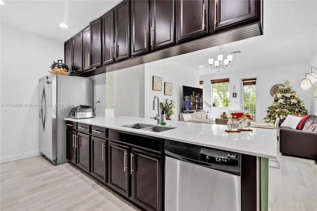 kitchen featuring appliances with stainless steel finishes, sink, kitchen peninsula, dark brown cabinets, and light wood-type flooring