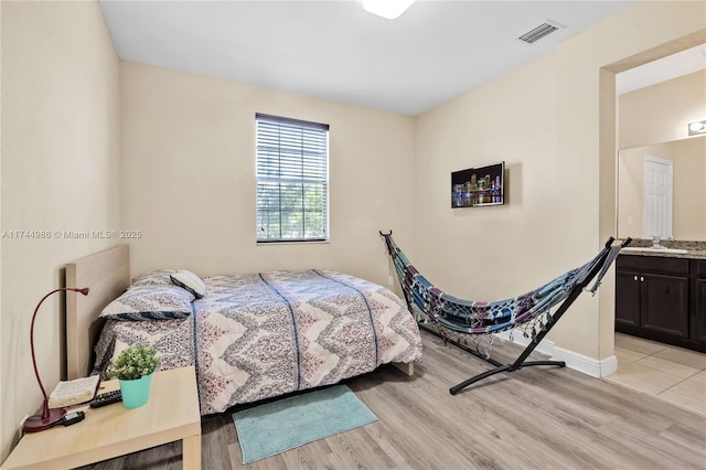 bedroom featuring light wood-style floors, visible vents, baseboards, and a sink
