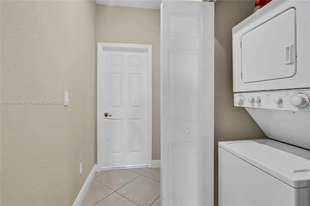 laundry room with stacked washer / dryer, laundry area, baseboards, and light tile patterned flooring