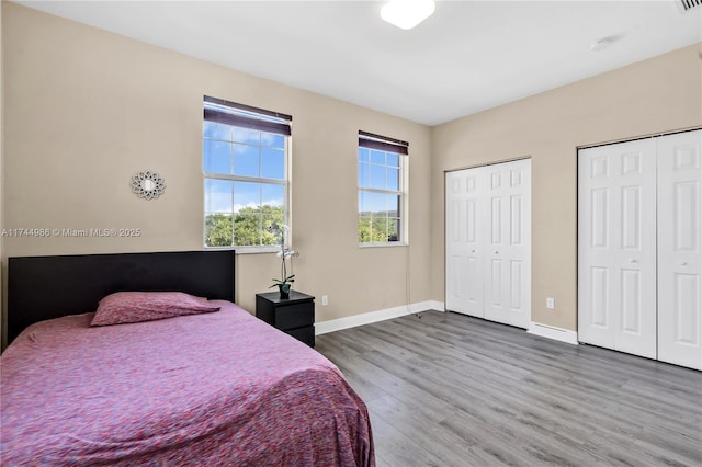bedroom featuring wood finished floors, baseboards, and multiple closets