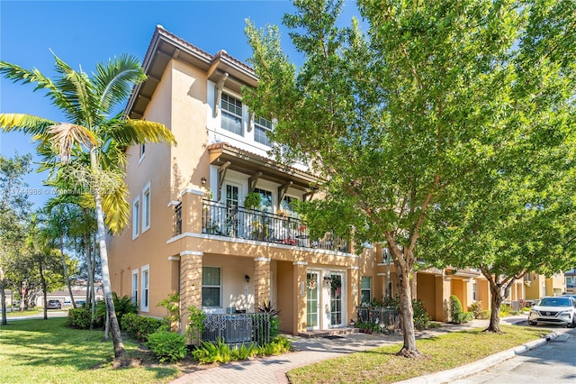 view of front of home featuring a front lawn, stucco siding, a tile roof, and a balcony