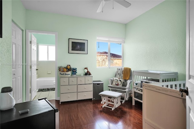 interior space with ceiling fan, ensuite bathroom, dark hardwood / wood-style floors, and a crib